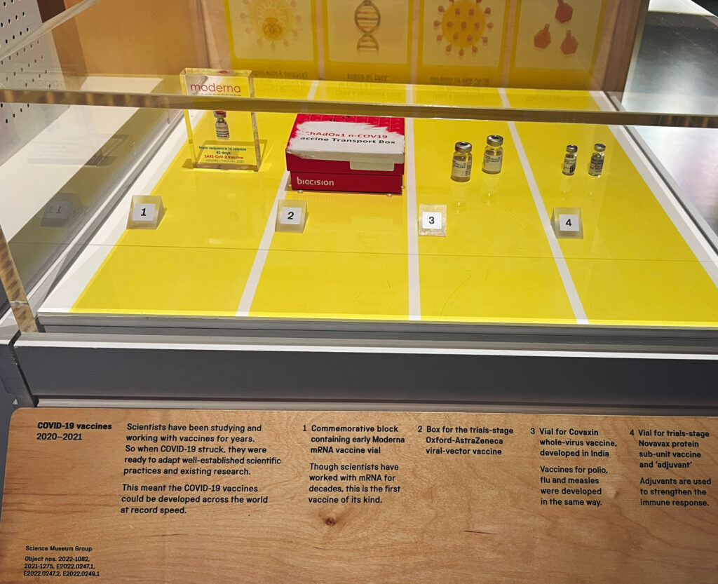 Photo of old vaccine vials in museum display case, with labels below.