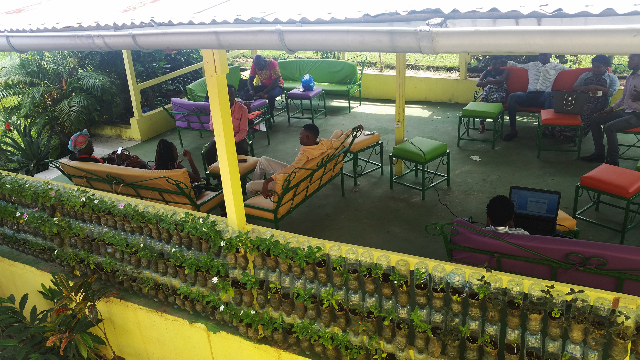 Overhead shot of colorful study space at auniversity in Gabon, with plants in plastic-bottle planters in the foreground, and an open space with students lounging on yellow sofas below