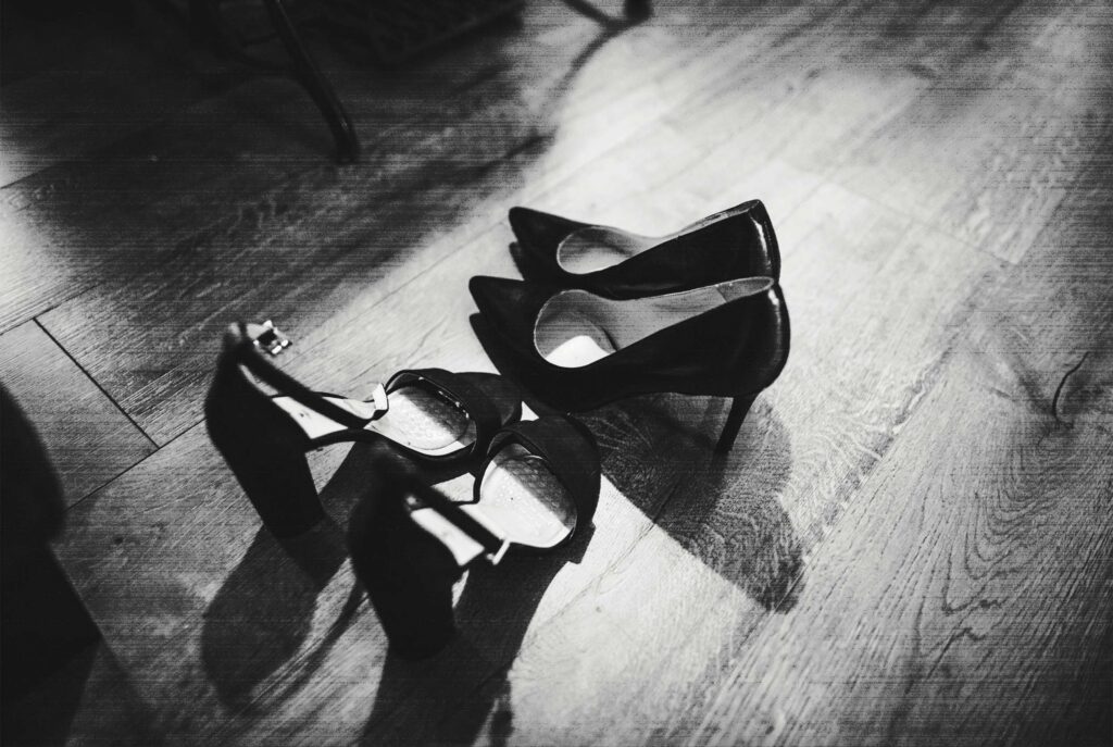 two pairs of high-heel shoes sitting on empty wood floor, in black and white