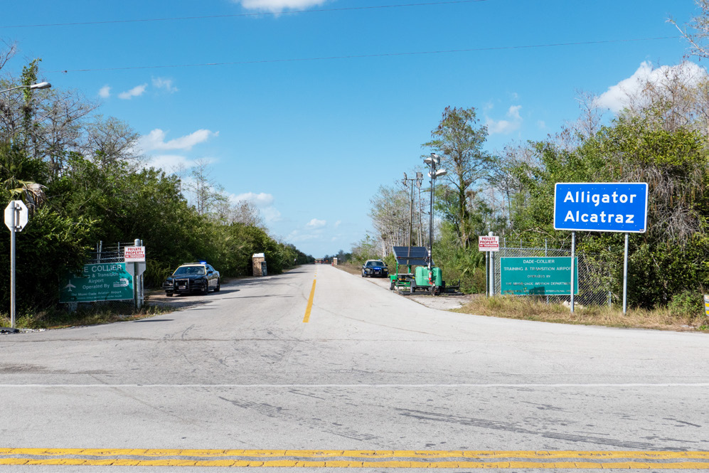 Road entrance to the Everglades Detention Center with an official road sign announcing the way to "Alligator Alcatraz."