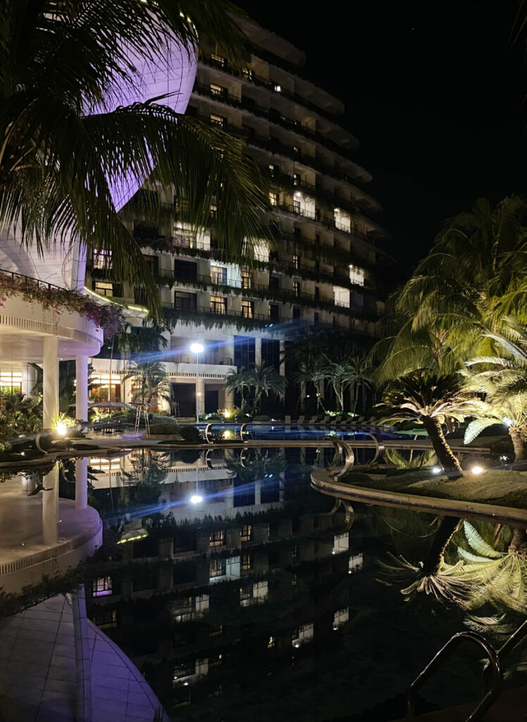 Marina Hotel pool at night, with lit-up rooms in a tall building and greenery nearby.